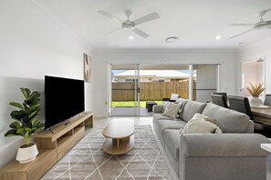 Un salon moderne avec un téléviseur à écran plat, un canapé gris, une table basse et un ventilateur de plafond.