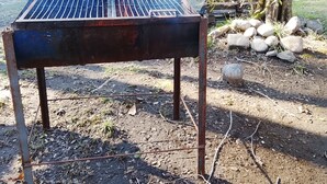 A metal grill outdoors with a river in the background. - Río Liucura Cabins for Two People (Pucón)