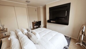 Een hotelkamer met een bed, een bureau, een stoel, een aan de muur bevestigde televisie en een kledingkast.