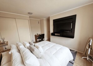 Een hotelkamer met een bed, een bureau, een stoel, een aan de muur bevestigde televisie en een kledingkast.