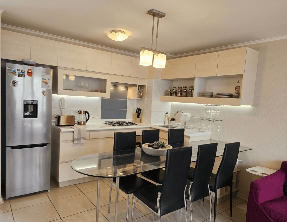 A modern kitchen with a stainless steel refrigerator, a glass dining table, and black chairs.