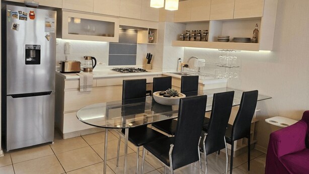 Een moderne keuken met een roestvrijstalen koelkast, een glazen eettafel en zwarte stoelen.