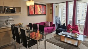 Een moderne woonkamer met een glazen eettafel, zwarte stoelen, een paarse bank en een salontafel.