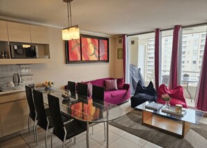 Een moderne woonkamer met een glazen eettafel, zwarte stoelen, een paarse bank en een salontafel.