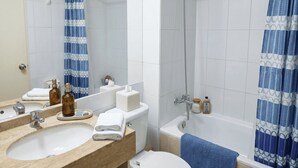 Een badkamer met een wastafel, spiegel, toilet, douche en een douchegordijn met een blauw-wit patroon.