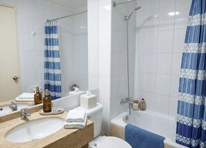 Een badkamer met een wastafel, spiegel, toilet, douche en een douchegordijn met een blauw-wit patroon.