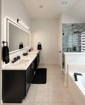 A modern bathroom with a double sink vanity, a large mirror with integrated lighting, a glass shower enclosure, and a black bath mat. - Spacious Allen home with 4 bedrooms, 2.5 baths, and a nearby pond. (Allen)