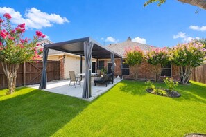 A backyard with a covered patio, a lawn, and a brick house. - Spacious Allen home with 4 bedrooms, 2.5 baths, and a nearby pond. (Allen)