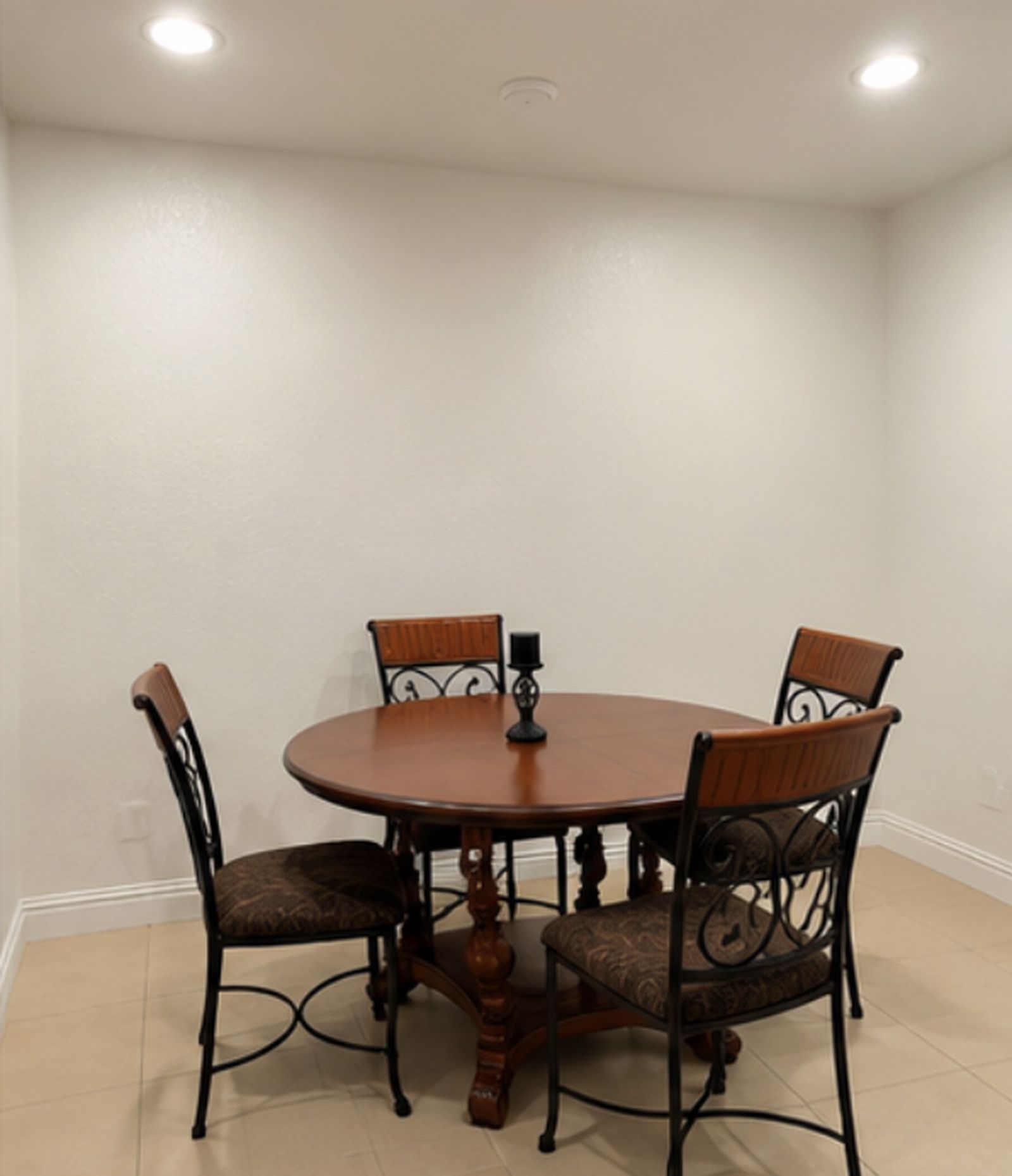 A dining table with four chairs, a candle, and a wall-mounted light fixture.