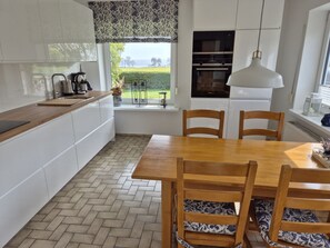 A modern kitchen with white cabinets, a wooden dining table, and chairs with patterned cushions. - Holiday Apartment With 2 Bedrooms (Fehmarn)
