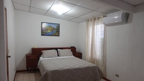 Un dormitorio con cama, mesitas de noche, un cuadro en la pared y un equipo de aire acondicionado.