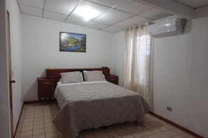 A bedroom with a bed, nightstands, a painting on the wall, and an air conditioning unit. - 4BR/4BA Comfortable Home with 2 Private Suites in Santa Tecla (Santa Tecla)
