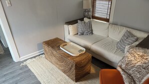 A living room with a sofa, a small ottoman with a tray, a lamp, and a window with blinds. - Welcoming 3-bedroom house in Asbury Park Close to Downtown & Beach (Asbury Park)