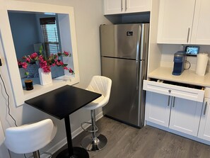 A modern kitchen with a stainless steel refrigerator, white cabinetry, a black countertop, and a window with a view.