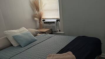 A bedroom with a bed, pillows, a bedside table with a lamp, and a window with blinds.
