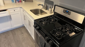 A kitchen with white cabinets, a stainless steel microwave, a black stove, and a stainless steel sink. - Welcoming 3-bedroom house in Asbury Park Close to Downtown & Beach (Asbury Park)