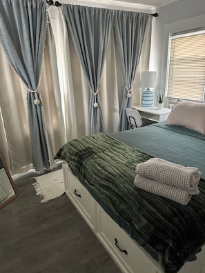 Ein Schlafzimmer mit Bett, Schreibtisch, Stuhl und Vorhängen.