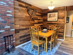 A dining area with a wooden table and chairs, a blue patterned rug, and a wall-mounted light fixture. - Penthouse. Sleeps9. 1K, 1Q Bdrms, 2 bath + loft w bunks at Seasons in BartlettNH (Bartlett)