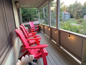 En inglasad veranda med röda Adirondack-stolar och ljusslingor.