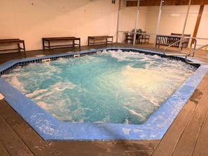 A hot tub with a wooden deck surrounding it, benches, and a table in the background. - Penthouse. Sleeps9. 1K, 1Q Bdrms, 2 bath + loft w bunks at Seasons in BartlettNH (Bartlett)