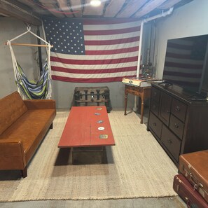 A room with a large American flag, a brown sofa, a red coffee table, a wooden cabinet, and a television. - Simpson Station: Historic Train Depot with direct access to recreational trails (Jay)