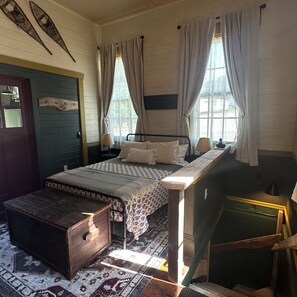 A room with a bed, a wooden chest, a desk, and a window with curtains. - Simpson Station: Historic Train Depot with direct access to recreational trails (Jay)