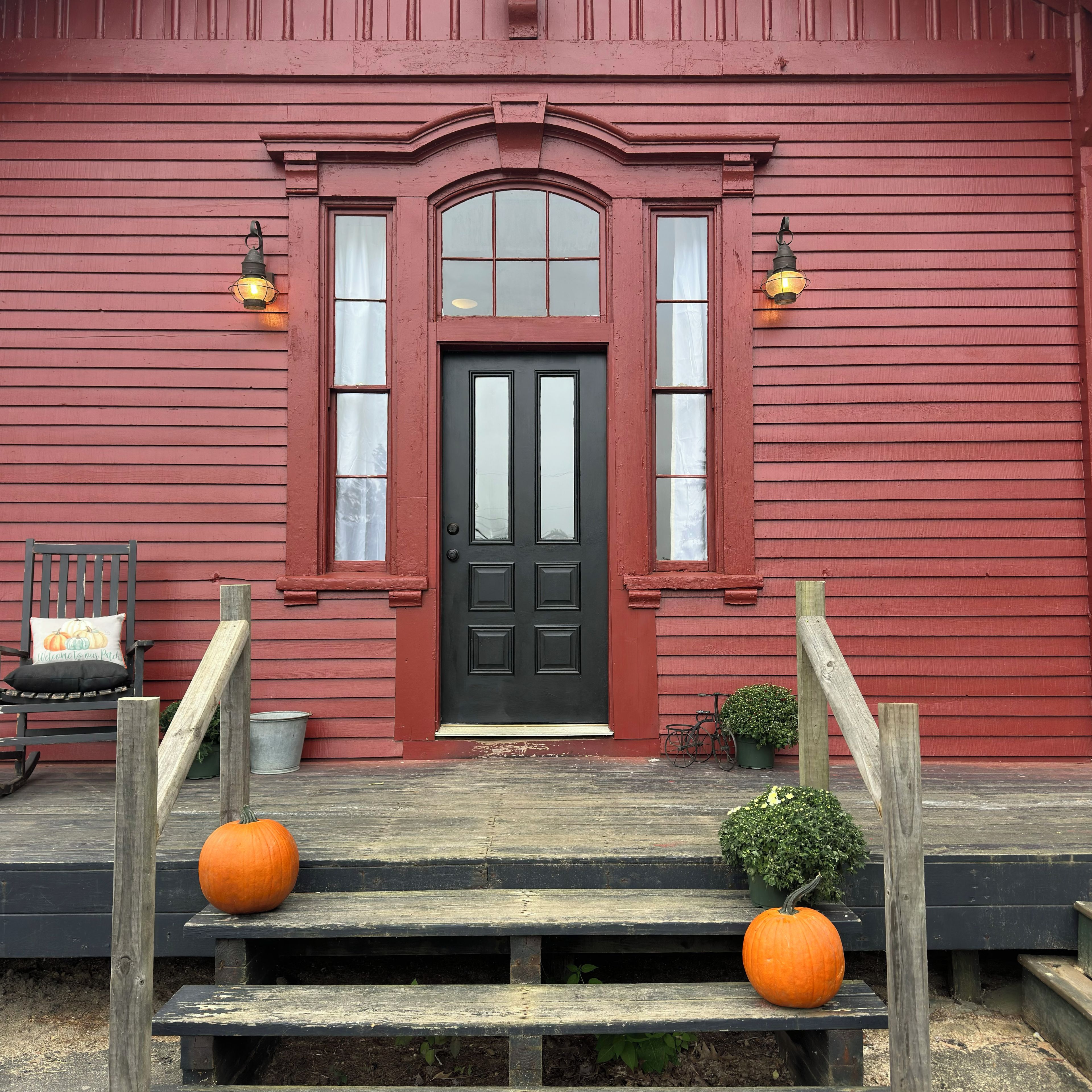 A red wooden building with a black door, two windows, and two wall-mounted lights.
