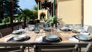 Un espace de restauration en plein air avec des tables dressées pour un repas, entouré de verdure et avec un bâtiment en arrière-plan.