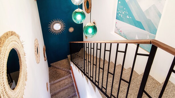 Un escalier avec une rampe en bois et des balustrades en métal noir, menant à une pièce dont un mur est peint en bleu foncé et qui est décorée d’œuvres d’art mural.