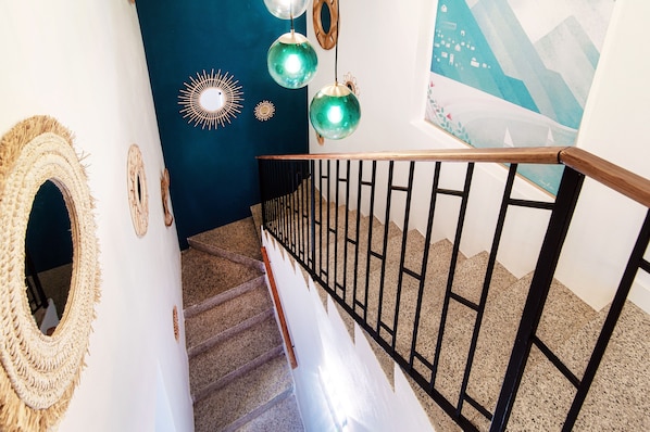 Una escalera con barandilla de madera y balaustres de metal negro, que conduce a una habitación con pared azul oscuro y decoración mural.