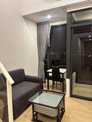 Uma sala de estar moderna com um sofá, uma mesa de centro de vidro e uma área de jantar com cadeiras.