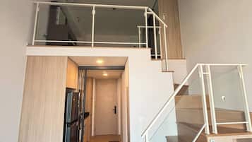 A modern interior with a staircase leading to a loft area, a kitchen with a refrigerator, and a door leading to another room.