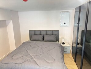 Quarto com cama, mesa de cabeceira, luminária e guarda-roupa.