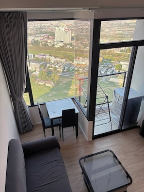 Uma sala de estar moderna com uma janela grande, um sofá, uma mesa de jantar com cadeiras e uma mesa pequena.