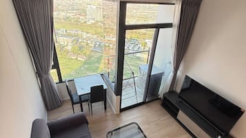 A modern living room with a sofa, a TV, a glass table, and a balcony with a view of a cityscape.