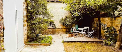 Un patio trasero con una terraza de madera, un pequeño jardín y un conjunto de asientos.