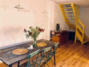 A dining area with a wooden table, chairs, a vase with flowers, and a yellow spiral staircase in the background. - Charming country house (Villiers-sous-Grez)