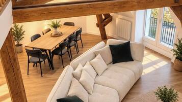 Un loft moderne avec des poutres apparentes, un canapé incurvé, une table à manger et des plantes en pot.