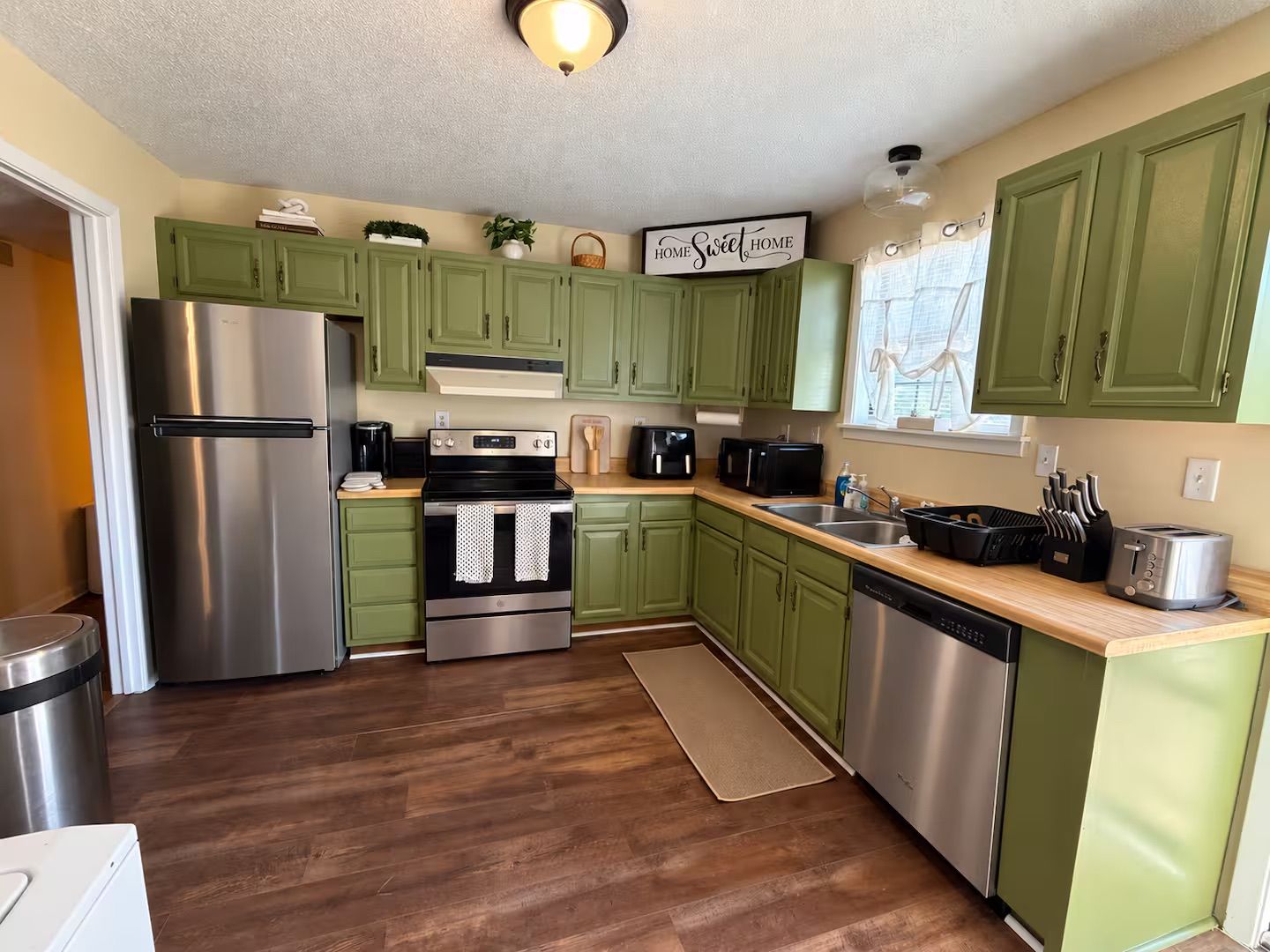 A kitchen with green cabinets, stainless steel appliances, and a 'Home Sweet Home' sign.