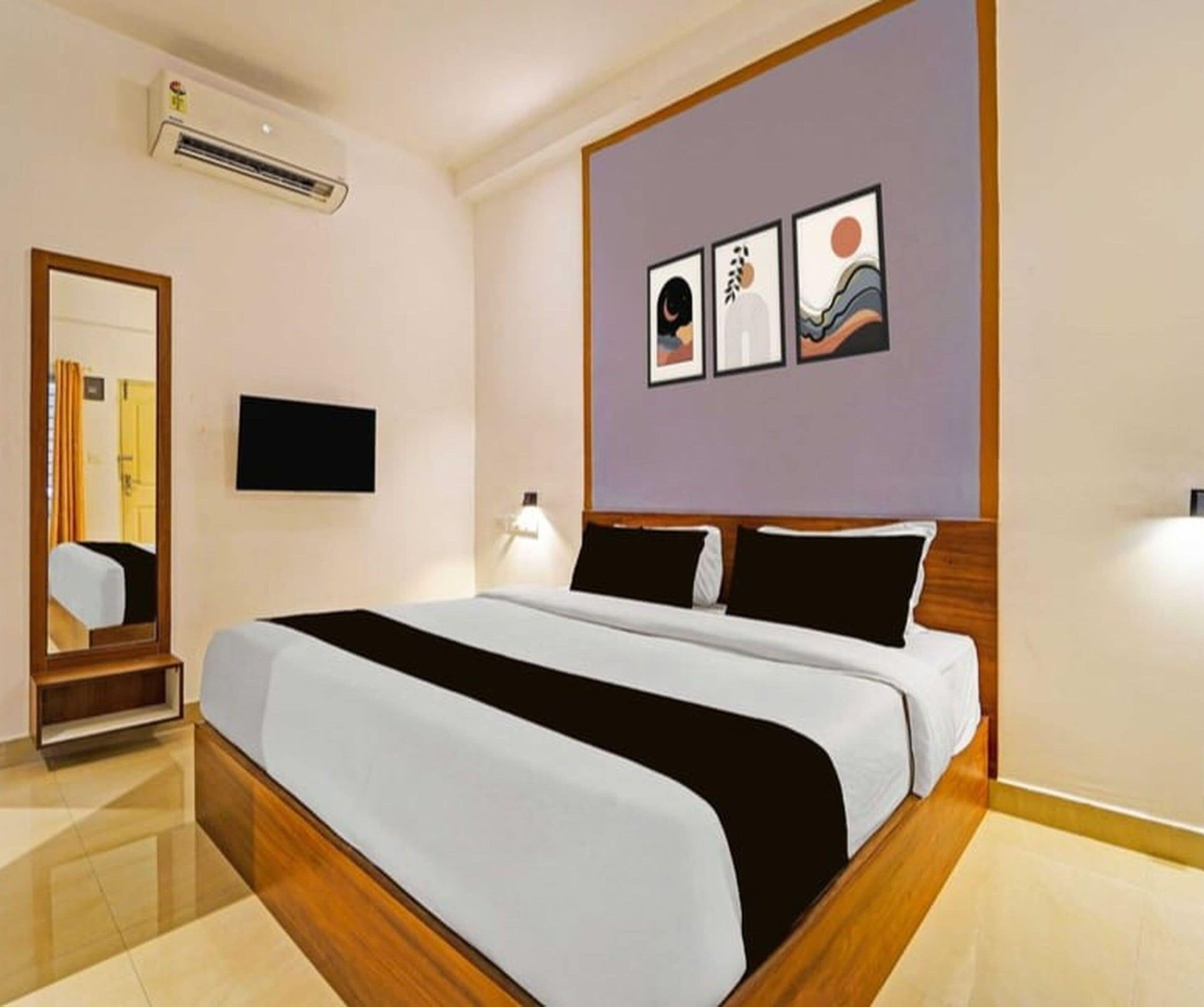 A hotel room with a bed, a flat-screen TV, a mirror, and artwork on the wall.