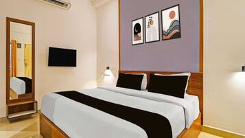 A hotel room with a bed, a flat-screen TV, a mirror, and artwork on the wall.