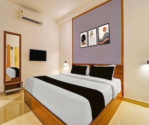 Hotellihuone, jossa on sänky, taulutelevisio, peili ja taideteoksia seinällä.