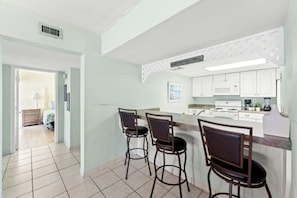 A kitchen with a central island, bar stools, and white cabinets. - Oceanfront 3BR- Brigadune I 17F- Pool (Myrtle Beach)