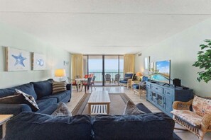 A hotel room with a balcony, a sofa, a dining table, and a television. - Oceanfront 3BR- Brigadune I 17F- Pool (Myrtle Beach)