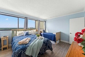 A bedroom with a large bed, a desk, a chair, and a view of the outdoors. - Oceanfront 3BR- Brigadune I 17F- Pool (Myrtle Beach)