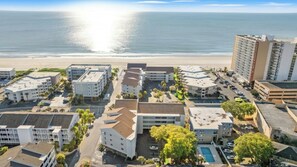 A coastal hotel complex with multiple buildings, a parking area, and a pool. - 3BR Pelicans Watch 110- Pool- 3BR In Shore Drive (Myrtle Beach)