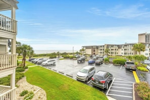 A parking lot with multiple cars, a grassy area, and buildings with balconies. - Ocean Forest Villas 213E- Outdoor Pool & Hot Tub (Myrtle Beach)
