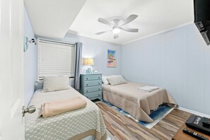 A bedroom with two beds, a ceiling fan, a bedside table with a lamp, and a painting on the wall. - Ocean Forest Villas 213E- Outdoor Pool & Hot Tub (Myrtle Beach)