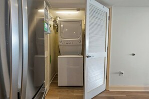 A laundry room with a washing machine and dryer, a door with a handle, and a light switch on the wall. - Bahama Sands Luxury PH3- 3 Bedrooms Oceanfront (North Myrtle Beach)