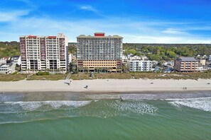 A beachfront hotel with multiple floors, a sandy beach in the foreground, and a clear sky. - Bahama Sands Luxury PH3- 3 Bedrooms Oceanfront (North Myrtle Beach)